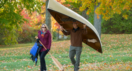 two people walking with one carrying a canoe