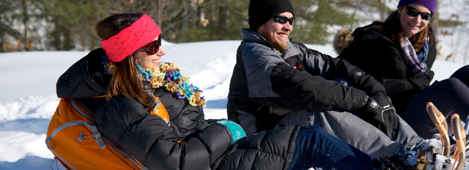 three people sitting in the snow wearing snowshoes